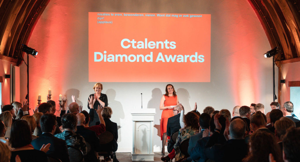 Een presentatie door een presentatrice en een tolk bij de Ctalents Diamond Awards in een kasteel. Het publiek klapt.