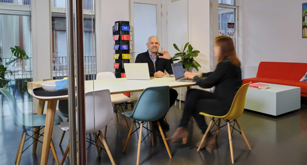 Een man heeft zijn hand omhoog en werkt samen met een vrouw aan een tafel