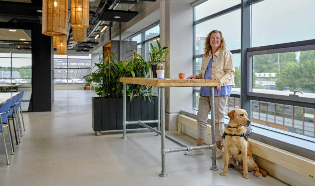 Een vrouw staat samen met haar hulphond aan een tafel