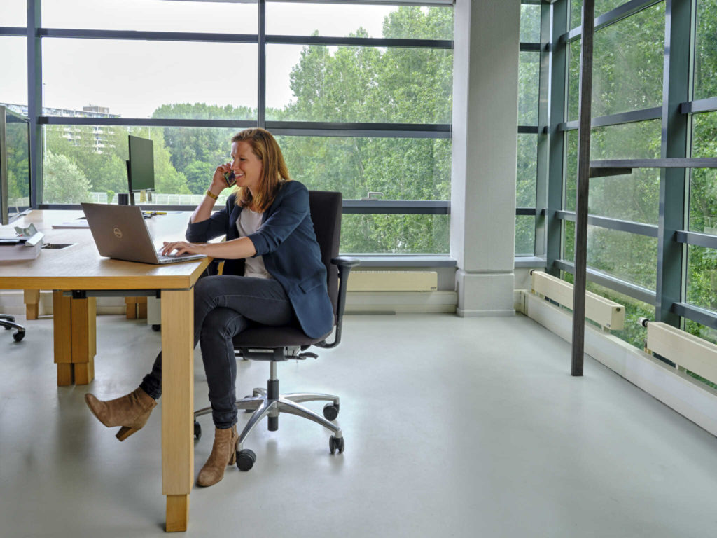 Een vrouw zit achter haar laptop te bellen en lacht