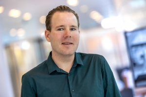 Foto van Stephan met een geblurde achtergrond. Hij draagt een zwart overhemd.