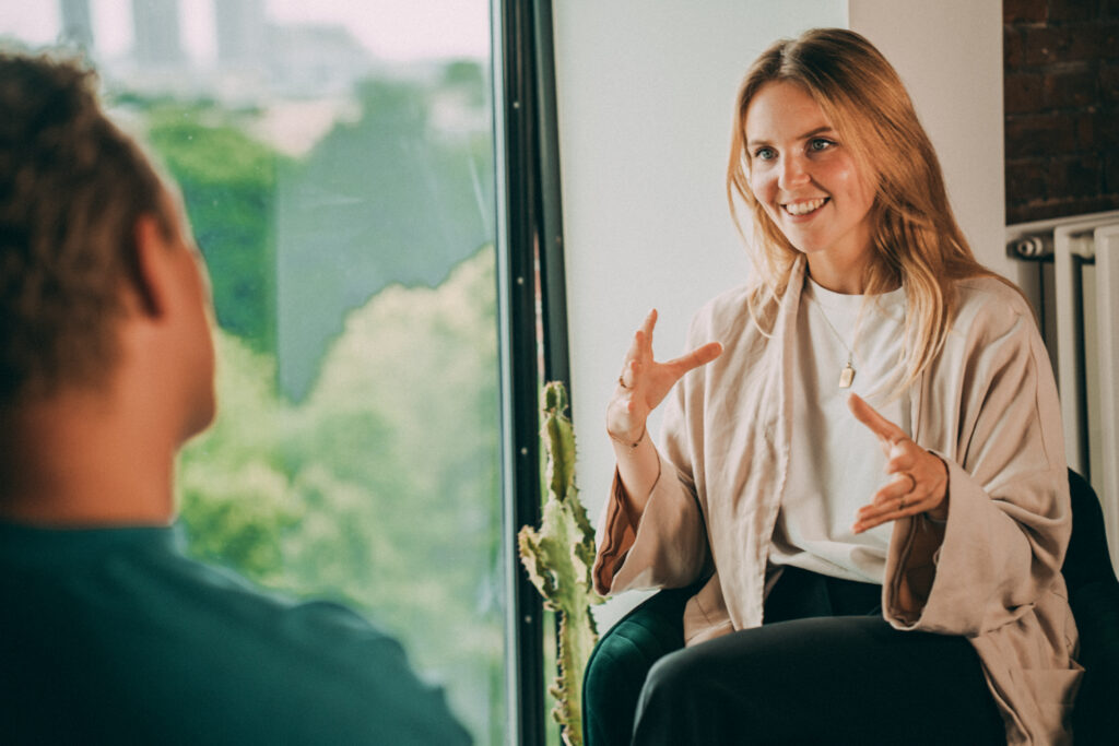 Een Ctalents-coach die in gesprek is. Ze heeft haar handen omhoog en glimlacht.