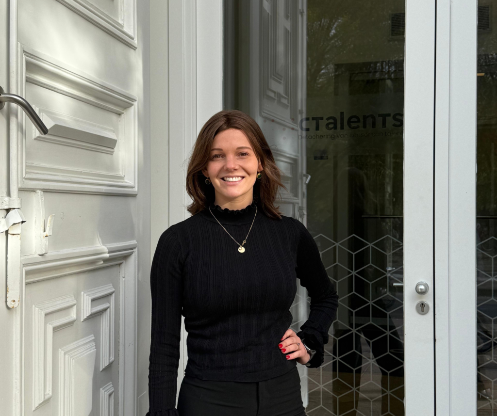 Een foto van Jolien die voor de deur van het Ctalents kantoor staat. Ze glimlacht en heeft haar hand op haar zij.