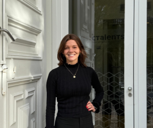 Een foto van Jolien die voor de deur van het Ctalents kantoor staat. Ze glimlacht en heeft haar hand op haar zij.