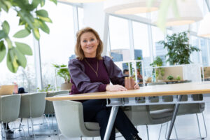 Een foto van Brechtje die naar de camera kijkt. Ze zit achter een tafel.